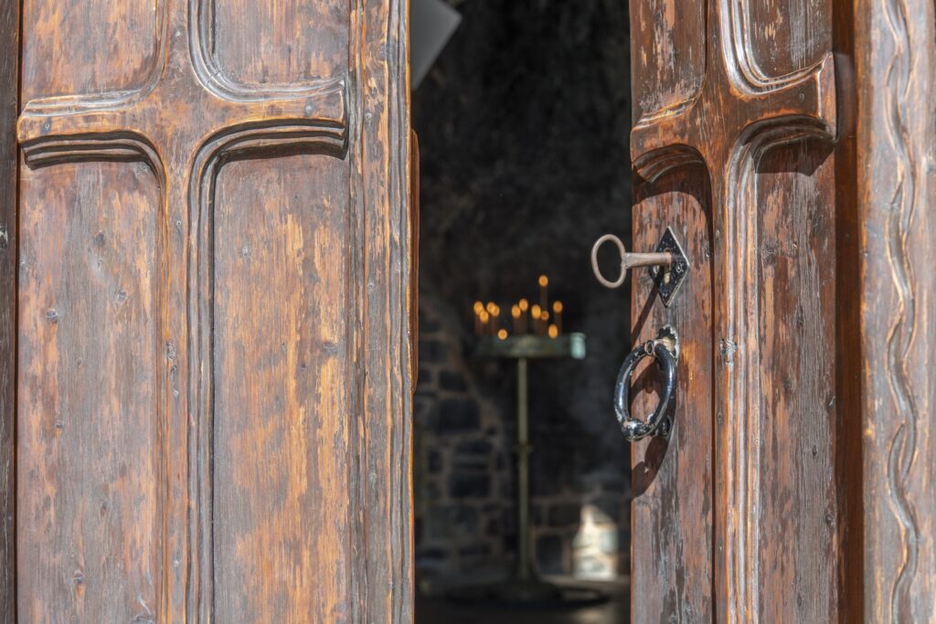 An open wooden door with a key in the lock, showing candles inside of a building.