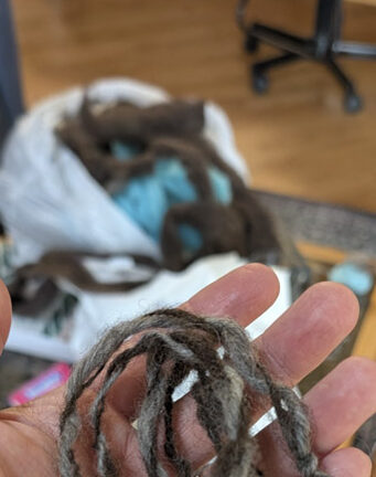 A handful of hand-made yarn, with a bag of raw wool in the background.